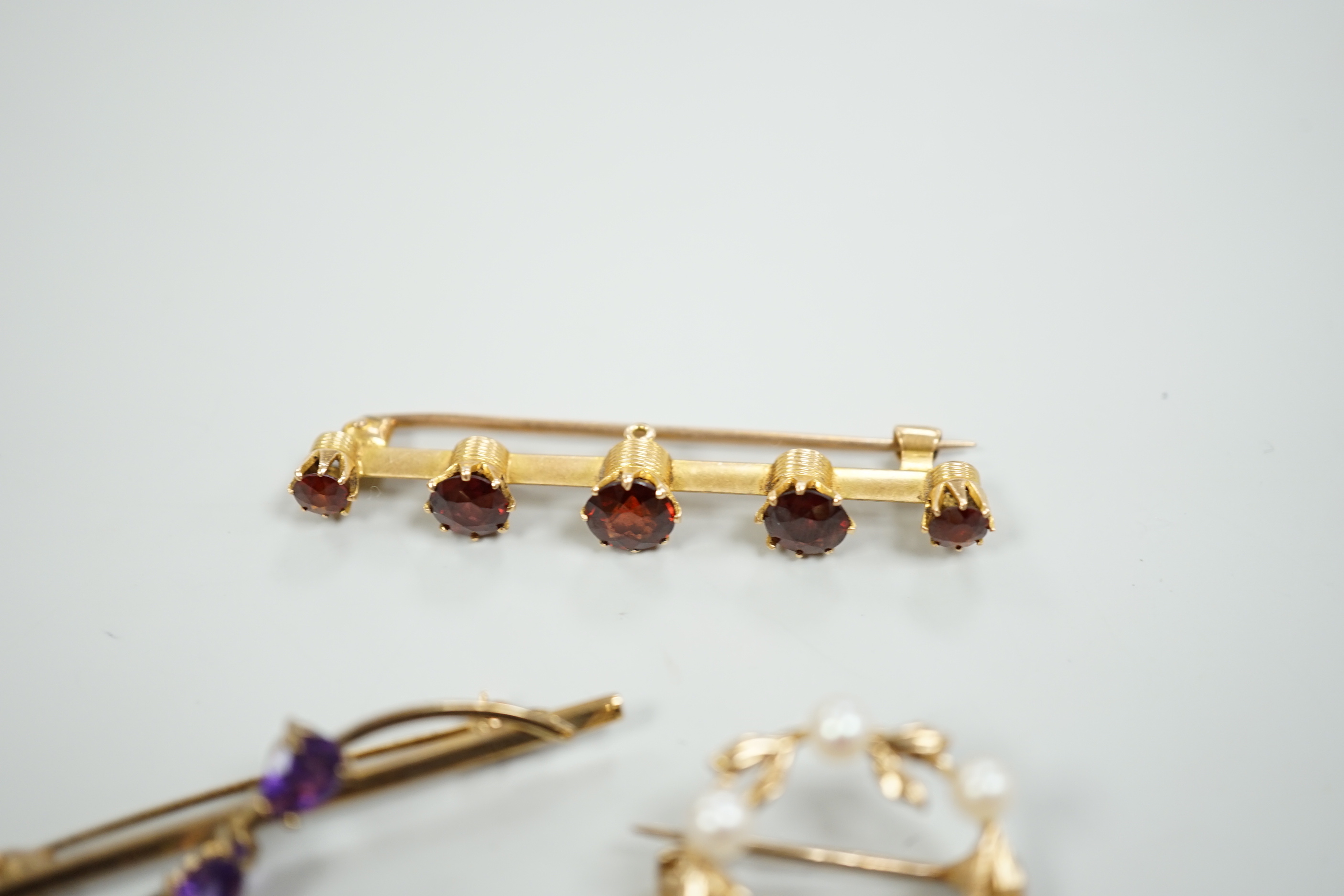 A 15ct and graduated five stone garnet set bar brooch, 48mm, a similar amethyst and seed pearl cluster set brooch and two other gem set brooches, including 9ct gold.